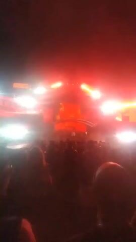 A crowd of people watch a stage at night. The stage has bright lights and a large logo that reads "THORR" in large yellow letters with a red background. There is smoke or fog on the stage. Some people are raising their hands.