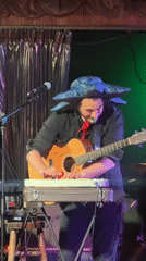 Acoustic guitarist performs in blue hat on London stage
