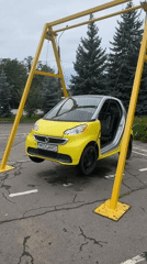 Yellow Smart car suspended from A-frame, swinging by cables