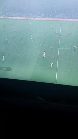 The video shows a person playing a soccer game on a television screen. The game is between Real Madrid and Rayo Vallecano. The score is 1-0 in favor of Real Madrid. The camera is pointed at the television screen from a low angle, making the top of the screen cut off. The person playing the game is not visible. The environment is dark, with only the light from the television screen illuminating the area.