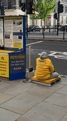 Person in Falun Dafa sweatshirt sits on London sidewalk