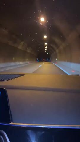 The video shows a first-person perspective of driving through a tunnel at night. The tunnel is illuminated by overhead lights, and there are cars in front. The car exits the tunnel and continues on a highway at night. Speed limit signs are visible.