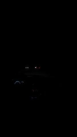 The video shows a car interior at night. Other cars are seen in the distance through the windshield, with their headlights visible. The dashboard gauges and radio of the car are lit up. A music track plays in the background.