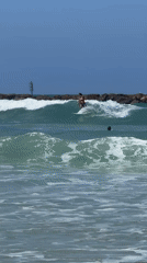 Surfer rides waves near Tel Aviv breakwater under clear skies