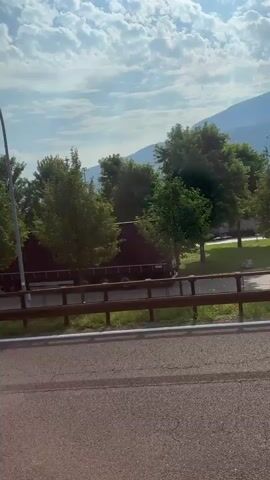 A truck with the Kogel logo is shown on a road. The truck appears to be under an overpass or bridge. Trees and a fence are visible in the background. The sky is cloudy.