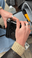 Person with camera bag observed wearing brown jacket, silver rings