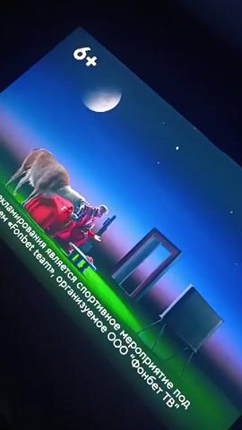 The video shows a screen displaying a promotional advertisement. A cartoon llama with a red bridle is prominently featured at the beginning of the video. Text appears on the screen, stating that this is advertising for a sporting event organized by OOO "Fonbet TV" under the name "Fonbet team." The scene transitions to a dark green background with several illuminated circles resembling spotlights on a stage or field. Within these circles, there are various figures. One circle contains a person in a white suit. Another contains a group of people seated at tables. A third shows people on a couch. The llama reappears in the lower right corner, alongside other figures. The overall impression is of a vibrant and energetic advertisement for a sports-related event.