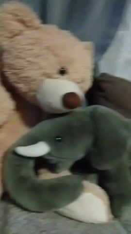 THIS VIDEO SHOWS A CLOSE-UP SHOT OF TWO STUFFED ANIMALS, A TAN BEAR AND A GREEN ELEPHANT, APPEARING TO BE EMBRACING EACH OTHER. THE BACKGROUND IS SOFTLY FOCUSED AND APPEARS TO BE INDOORS WITH TEXTURED SURFACES SUGGESTING FURNITURE OR CURTAINS. THE LIGHTING IS DIM AND WARM. THE STUFFED ANIMALS ARE POSITIONED TOGETHER, WITH THE BEAR'S HEAD RESTING ON OR NEAR THE ELEPHANT'S TRUNK AND HEAD. THERE IS NO AUDIO PRESENT IN THE VIDEO.