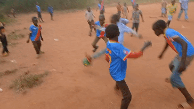 Children play soccer on dirt field in rural Congo