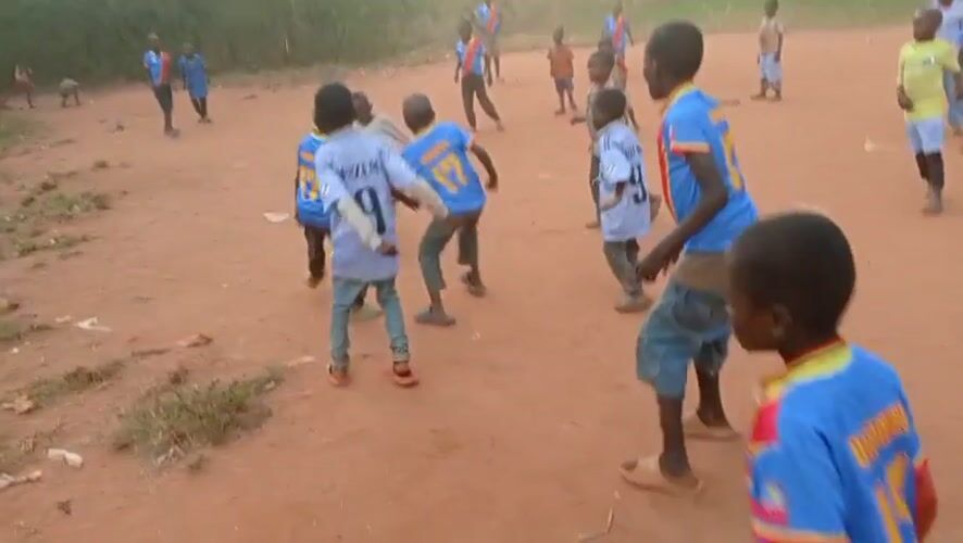 Children play soccer on dirt field in rural Congo