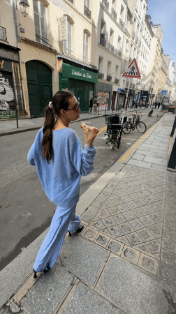 Woman in light blue spotted eating, walking in Paris