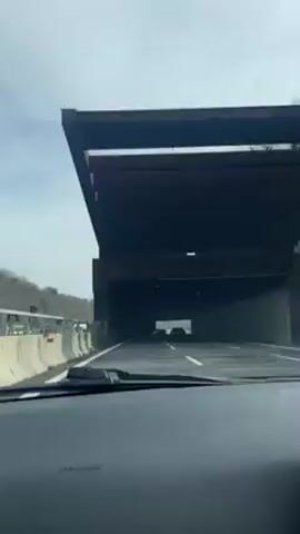 A car is driving into a tunnel. The tunnel has a concrete ceiling and lights above. There are other cars in front. The video is shot from the driver's seat.