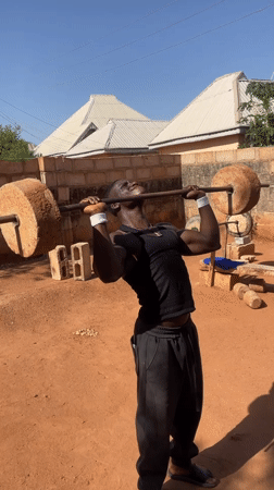 Young man performs weightlifting exercise with stone weights in Bukuru