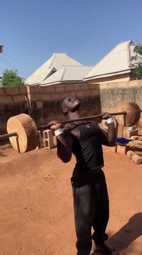 Young man performs weightlifting exercise with stone weights in Bukuru