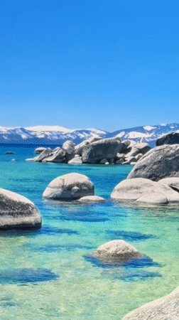 Turquoise lake with grey boulders and snow-capped backdrop
