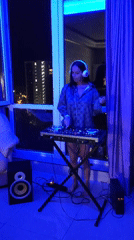 Woman DJs barefoot in blue-lit Sochi apartment overlooking cityscape