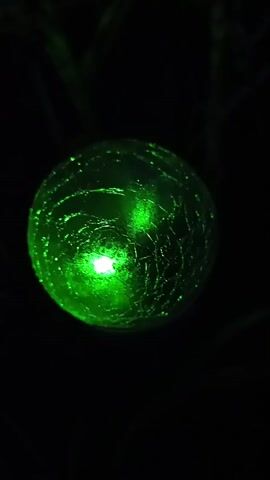 A green light emanates from a cracked sphere against a black background. The light shifts to red, then red with yellow hues, and then back to red. The sphere is round and has a textured, broken surface.