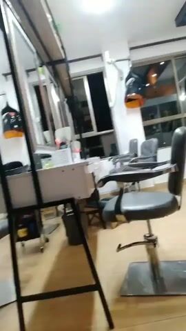 The video shows the interior of a hair salon. The lighting is bright. There are several styling chairs, a reception desk, and a large mirror. The floor is tiled. There are products on shelves behind the reception desk. A sign on the wall says "Beauty Sol Salon & Spa". The camera pans across the room, showing different angles of the salon. In some shots, the camera is focused on a black styling chair, while in others, it shows the entire room. The video is shaky at times, suggesting it may have been filmed by hand. There are no people clearly visible in the video, although there might be a person's leg in the bottom corner of the frame in some shots. The overall impression is that of a clean and well-equipped salon.