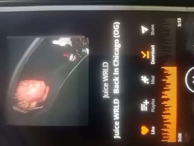 The video shows a phone screen with music playing. The song is by Juice WRLD and is titled "Back In Chicago (OG)". The album art is a picture of Juice WRLD. The song is 3:08 long and has a duration of 5:13. The screen also shows options to like, add to playlist, modify, download, and share the song. There is a progress bar indicating the song is playing. The phone is being held vertically and the screen is slightly tilted.