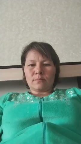 A woman with short brown hair is looking at the camera. She is wearing a green zipper jacket with a pattern on the chest. The background is a beige textured wall. She makes a few different facial expressions, including smiling and opening her mouth in surprise.