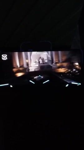 A phone screen is being recorded. The screen is showing a video of a dark, indoor space, then it shifts to a blue scene with a red light. The video then shows a blue scene of people walking on a beach near the ocean.