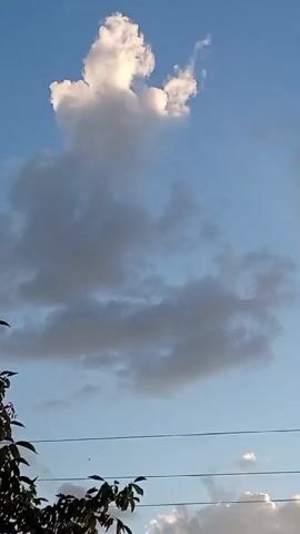 The video shows a time-lapse of clouds moving across a blue sky. There are some trees visible in the foreground and some power lines. The sun is setting, casting a warm glow on the clouds.