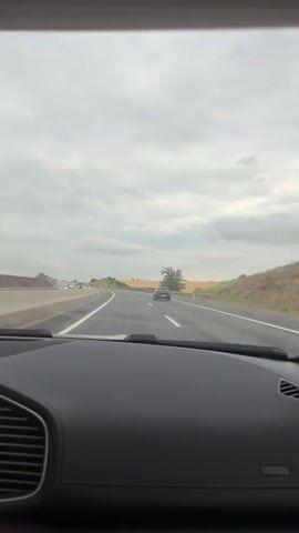 This video shows a first-person perspective from inside a car driving on a highway. The scene is a highway with multiple lanes, bordered by a guardrail on the left and fields on the right. There are other vehicles on the road, including cars and trucks. The weather appears to be overcast, with a cloudy sky. The overall mood is neutral, as the focus is on the act of driving and the passing scenery. There is no visible text in the video. The context provided indicates the location is Bullendorf, Austria. The activity is driving on a highway.