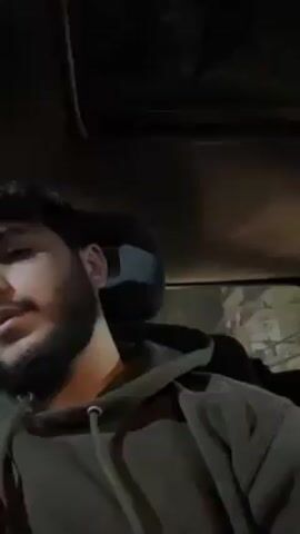 The video shows a person with a beard and a gray hoodie inside a car. The interior of the car is dark, with a view of the ceiling. The person appears to be speaking. The environment outside the car is dimly lit.