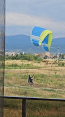 Paraglider launches from a field with a city backdrop