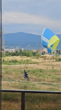 Paraglider launches from a field with a city backdrop