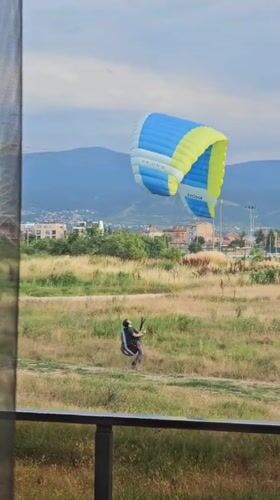 Paraglider launches from a field with a city backdrop