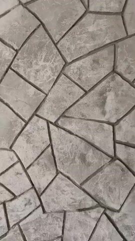 The video shows a close-up, vertical pan of a wall constructed with irregular, angular stones. The stones are light gray with darker gray grout lines separating them. The surface of the stones has a textured, somewhat rough appearance, with variations in shading and some finer crack-like markings. The lighting suggests an indoor environment or an overcast day, as there are no harsh shadows. The camera moves slowly downwards, revealing more of the stone pattern. No people or other objects are visible in the frame.