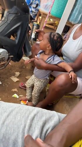 Woman holds baby and Guinness can in Kurunduma, Nigeria