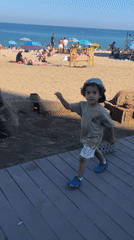 Child explores sand sculpture at busy Barcelona beach cafe