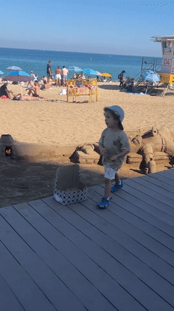 Child explores sand sculpture at busy Barcelona beach cafe