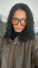 Person in brown jacket takes selfies, walks São Paulo streets