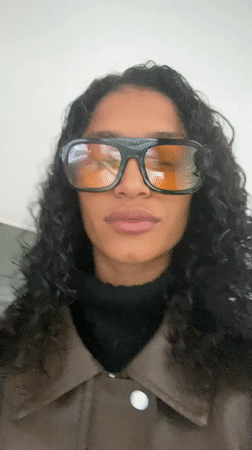 Person in brown jacket takes selfies, walks São Paulo streets