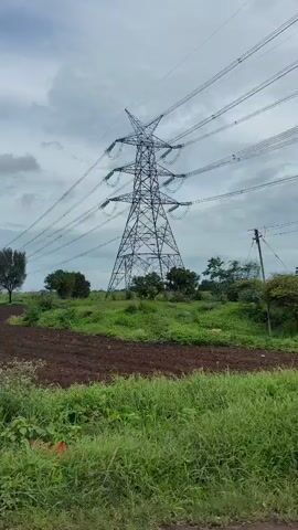 A view of a pylon and power lines over a rural landscape. The pylon is tall and metallic, with power lines stretching across the frame. The ground is covered in grass and some trees. The sky is cloudy. The camera appears to be moving horizontally, showing different sections of the landscape.