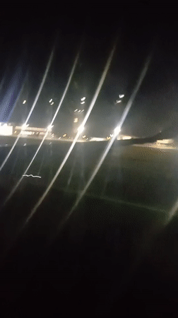 Nighttime airplane window view shows wing, ground lights