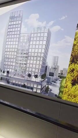 The video shows a moving walkway, likely in an airport or convention center. The walkway has a gray striped surface and glass sides with white lights underneath. A large advertisement for "Smarter steels for people and planet" is displayed on the wall beside the walkway, featuring architectural renderings of a modern building. A man wearing a backpack is walking on the walkway away from the camera. The environment appears clean and well-lit.