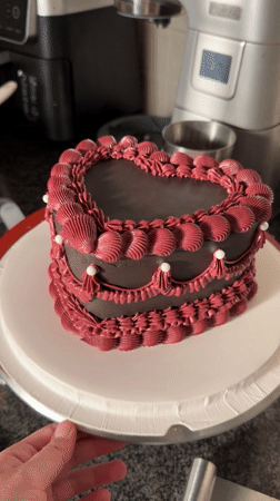 Woman decorates heart-shaped chocolate cake with Russian text in Tel-Aviv