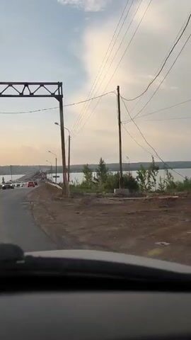 The video shows a car driving on a dirt road toward a bridge. The bridge appears to be over a body of water. A road sign indicates the direction of "Chusovaya".  The sky is cloudy and the setting appears to be rural.