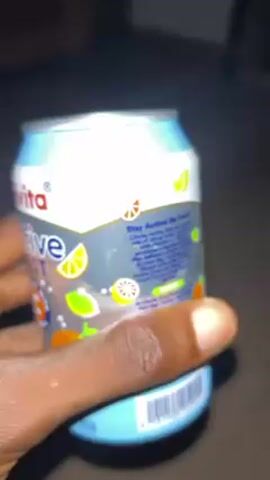 A person's hand holds and rotates a blue and white can of Chivita Active Zest mixed fruit drink. The can is adorned with images of various citrus fruits, including oranges, grapefruits, and lemons. The person is in a dimly lit environment, likely indoors.