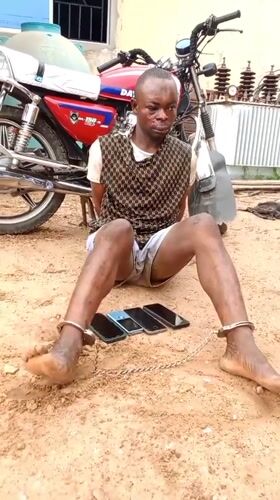 Restrained person sits on ground beside four laid-out phones