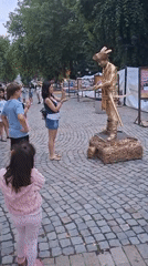 Gold living statue performer holds still on cobblestone street