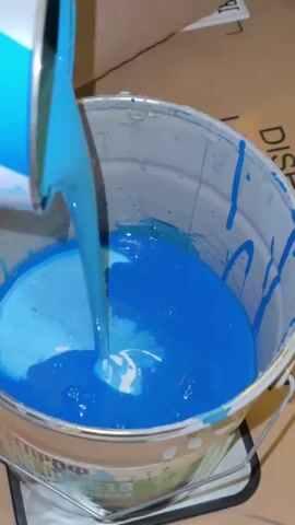 A close-up shot shows blue paint being poured from a can into a larger bucket of blue paint. The paint creates swirling patterns as it mixes.