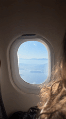 Passenger films mountain range and water from airplane window