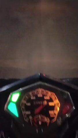 The video displays a close-up view of a motorcycle's instrument cluster. The speedometer needle is positioned slightly above 60 km/h, indicating the motorcycle is in motion. The odometer reads 74962. A green indicator light is illuminated on the left side of the instrument cluster, and an orange-red light is illuminated on the right. The background is blurred, suggesting movement.