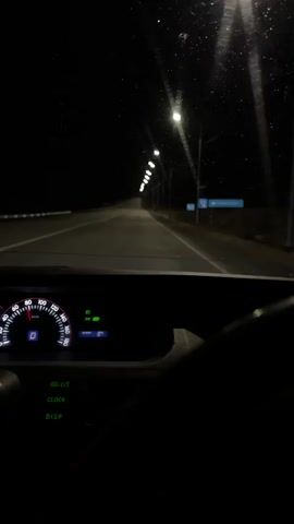 The video depicts a nighttime car journey. The view is from inside the vehicle, looking out through the windshield. Streetlights illuminate a straight, empty road ahead. The car's dashboard is visible, showing a speedometer reading approximately 90 km/h, indicator lights, and an outside temperature of 8 degrees Celsius. The interior is dark, with only the dashboard lights providing illumination.