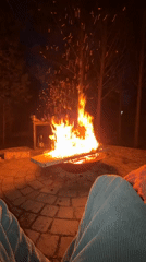 Person sits by nighttime fire pit in Манский, Russia